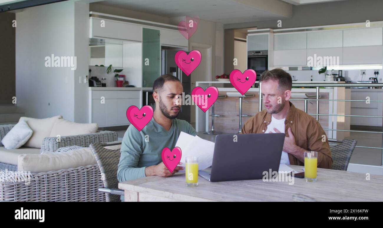 Image of heart icons over diverse gay couple using laptop Stock Photo