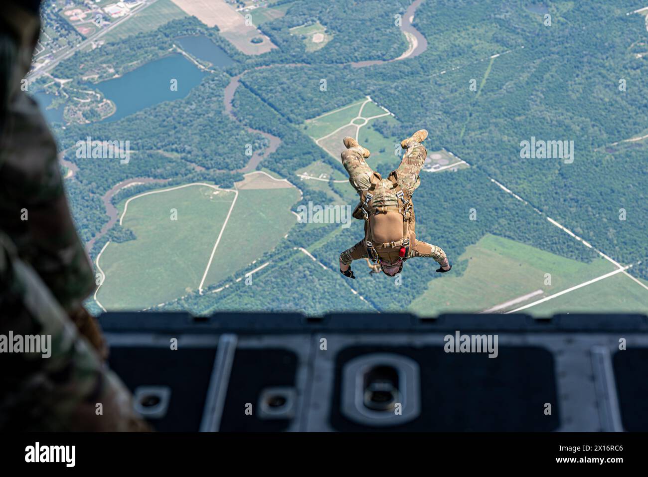 A man is doing a parachute jump from a plane. The scene is captured from the side of the plane Stock Photo