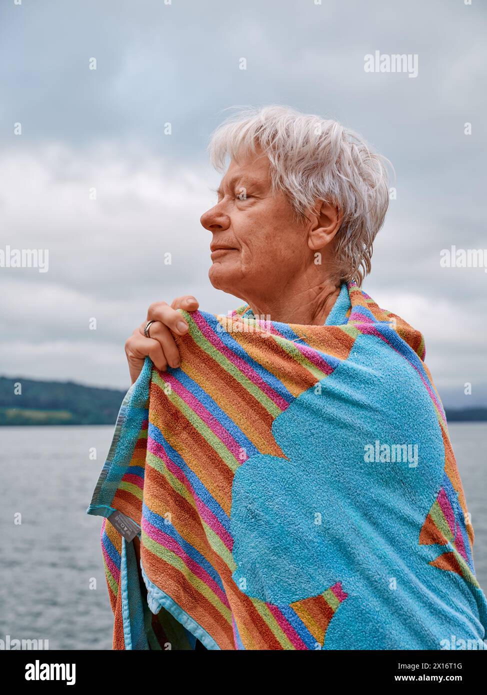 A senior open water wild swimmer warms themselves up with a towel after a refreshing cold water lake swim - woman swim outdoors health UK Stock Photo