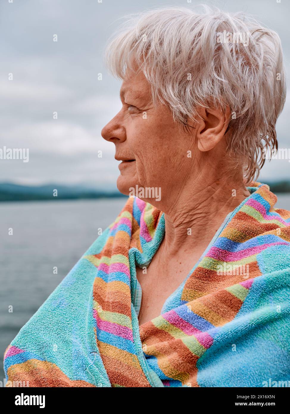 A senior open water wild swimmer warms themselves up with a towel after a refreshing cold water lake swim - woman swim outdoors health UK Stock Photo