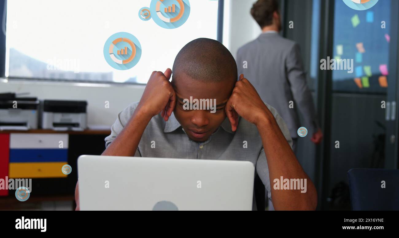 Image of multiple graph icons over tired african american man looking at laptop in office Stock Photo