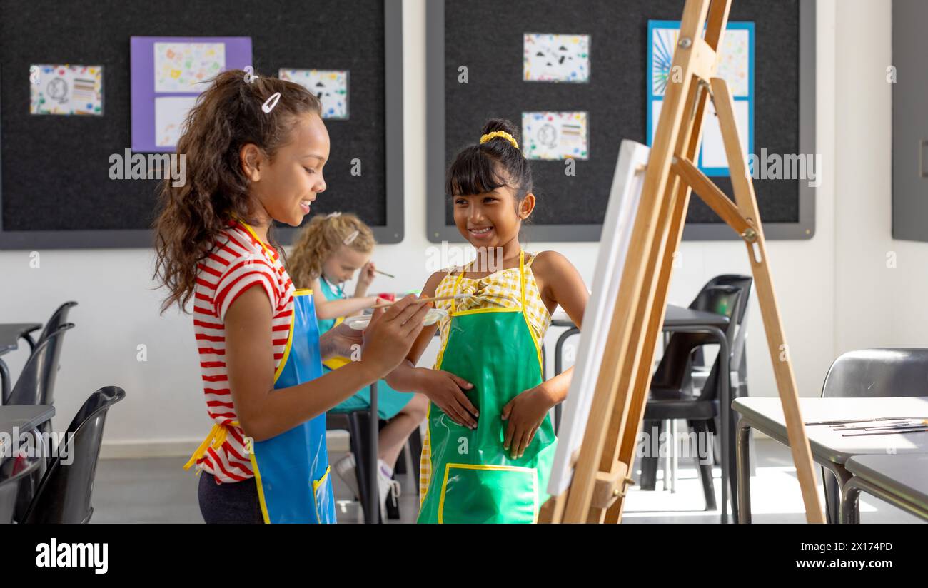 In school, in art class, a diverse group of young girls are painting ...