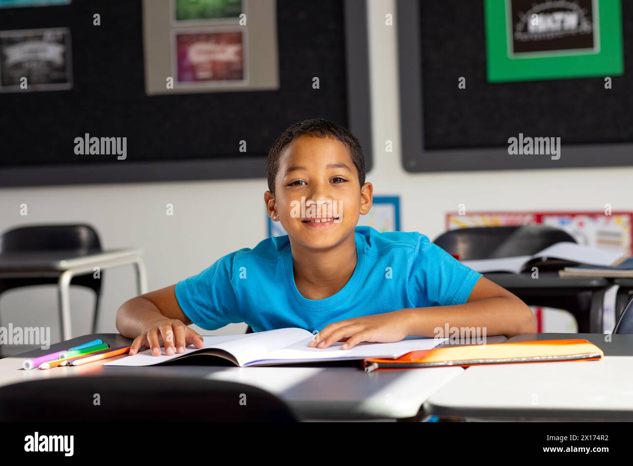 In school, young biracial male student sitting at a desk in a classroom ...