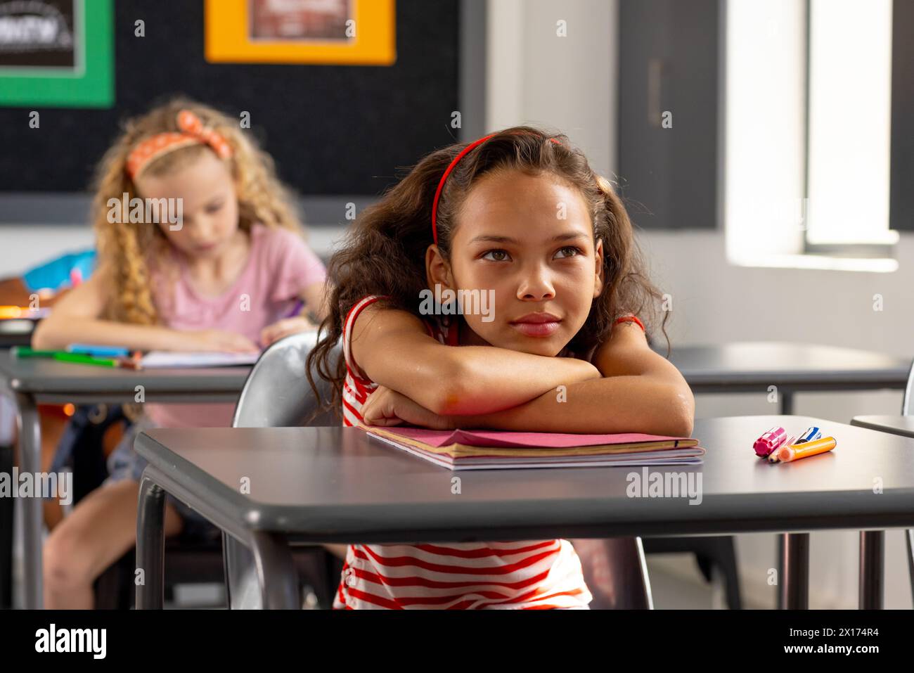 In school, young biracial female student sitting at a desk in a classroom, looking thoughtful Stock Photo