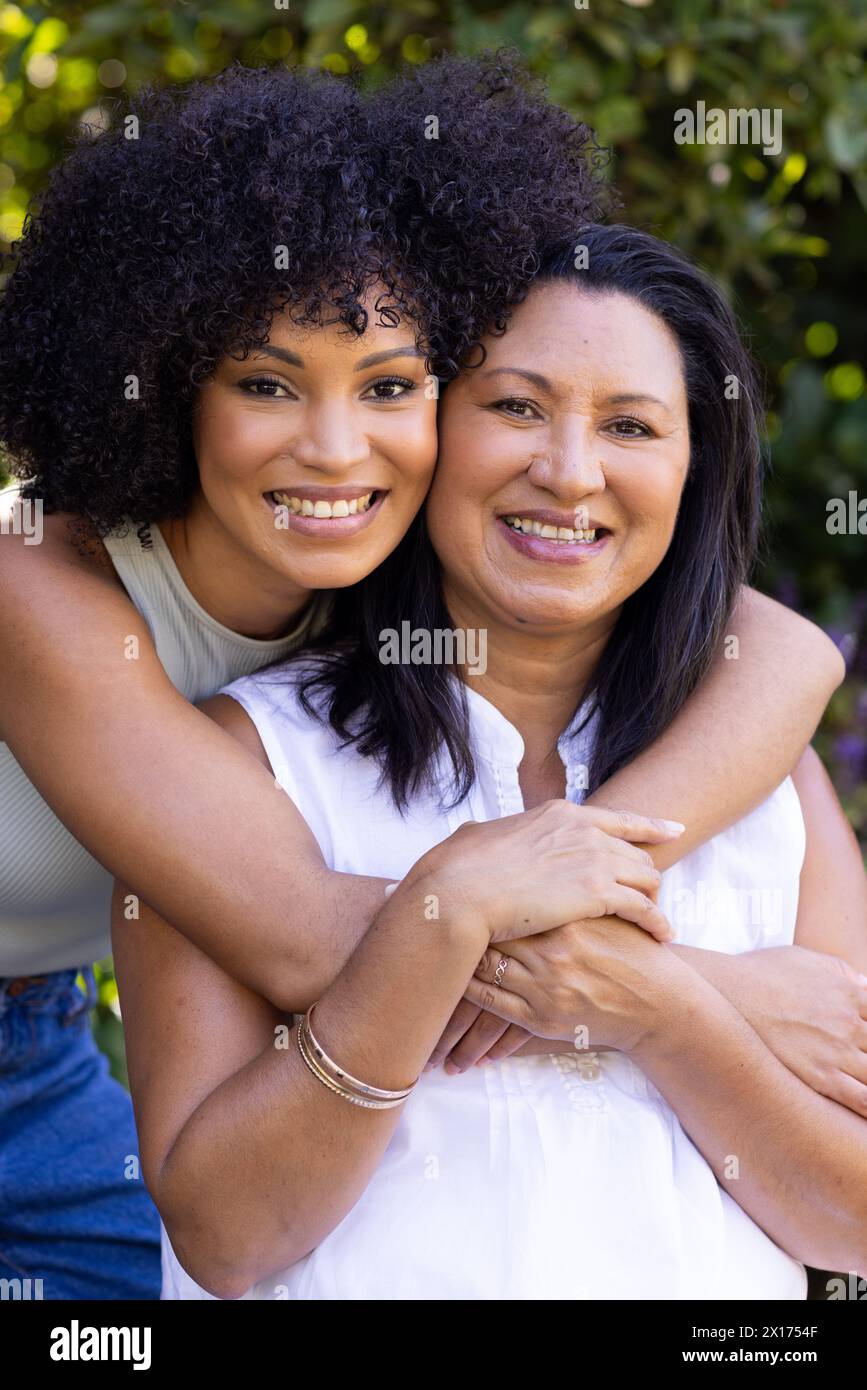Biracial mother and adult daughter are hugging, smiling outdoors at home in the garden Stock Photo