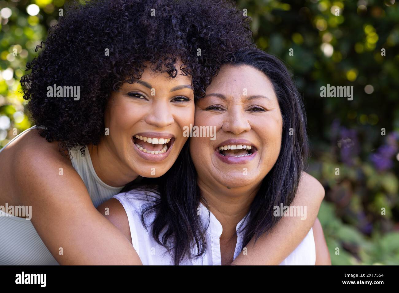 Biracial mother and adult daughter are laughing together outdoors at home in the garden Stock Photo