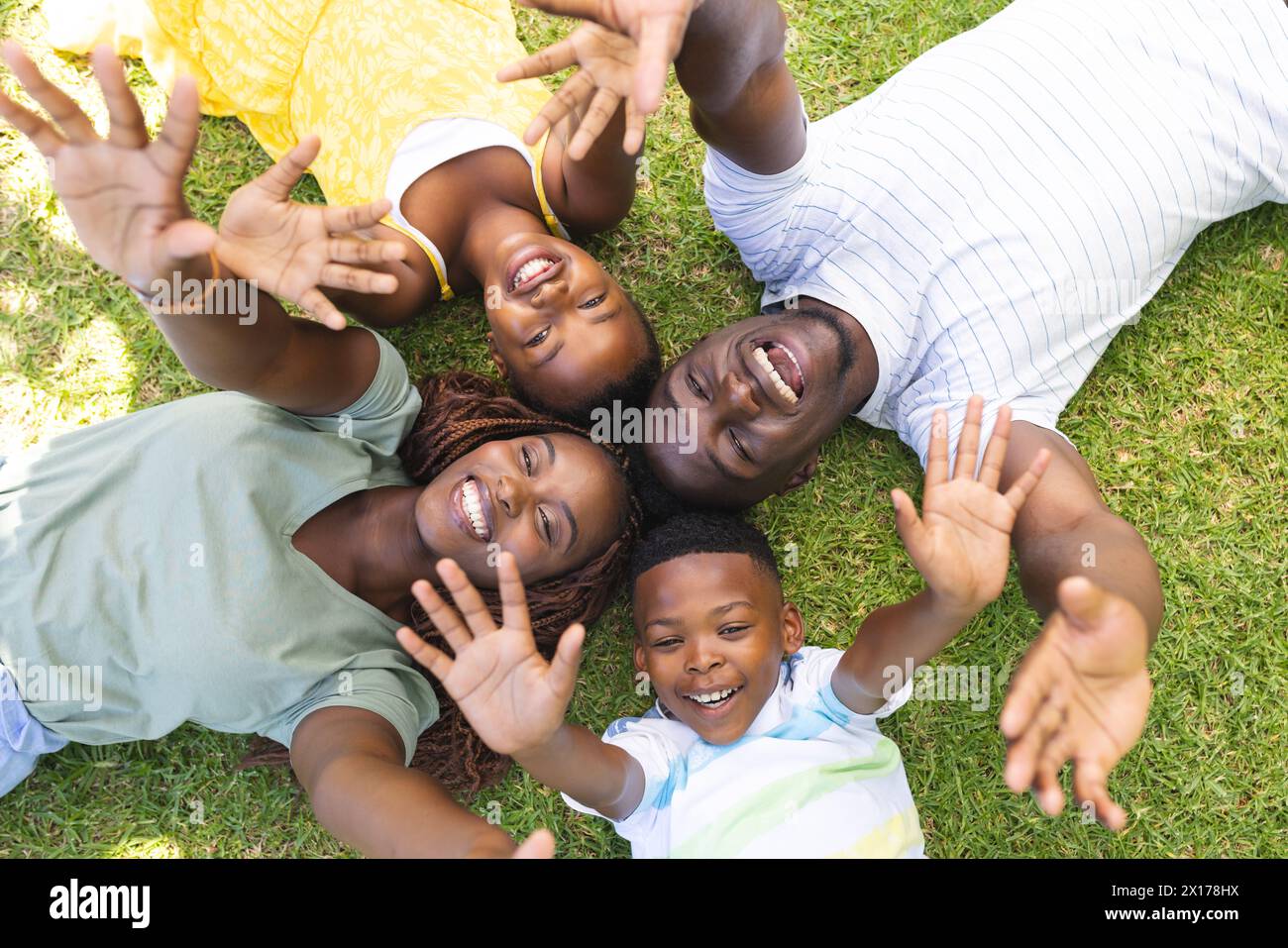 African American family lying on grass, waving at camera, enjoying time together Stock Photo
