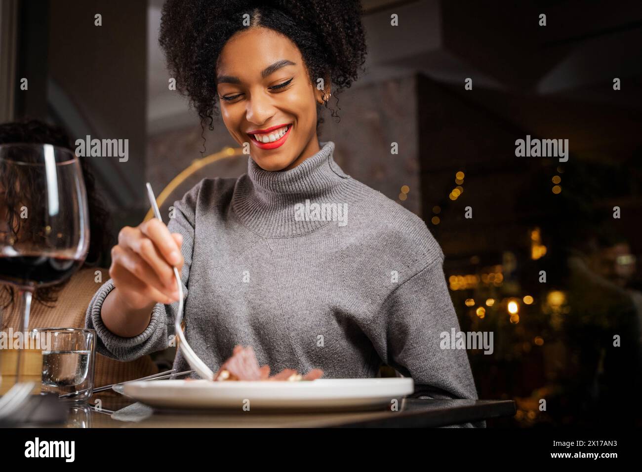 Smiling woman enjoying a gourmet meal at a fine dining restaurant - glass of red wine enhance the culinary experience - Elegance and satisfaction in a Stock Photo