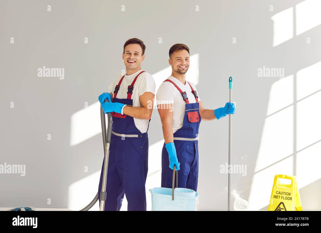 Portrait of two happy, smiling male janitors in uniforms with cleaning equipment Stock Photo