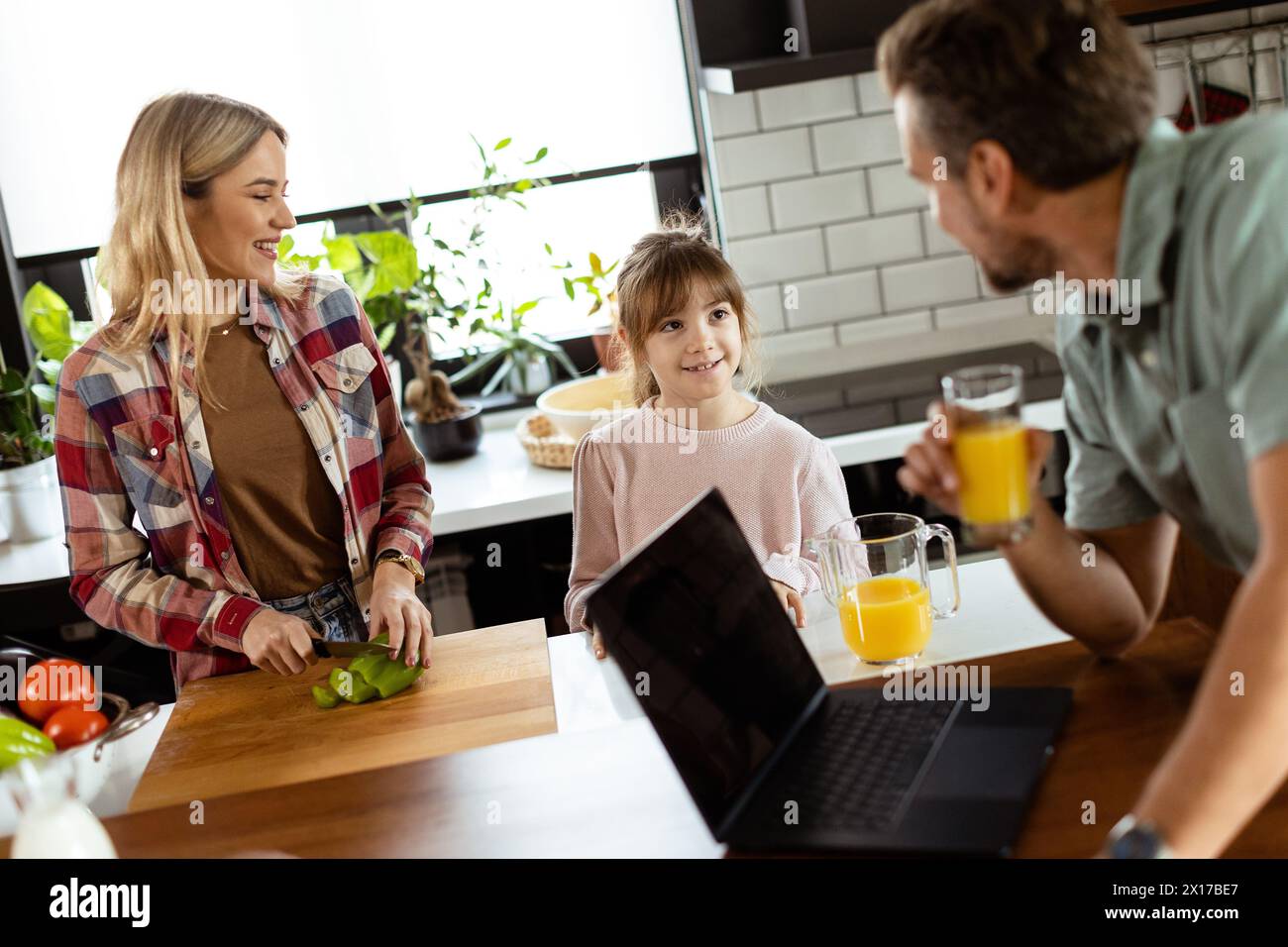 A cheerful family enjoys a warm conversation in their kitchen with fresh juice and a laptop sitting on the table. Stock Photo