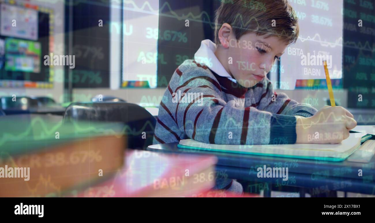 Image of trading board over caucasian boy writing in book at classroom Stock Photo