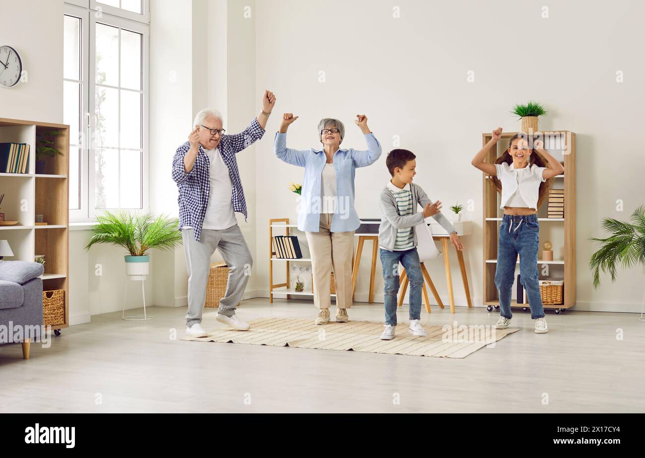 Funny senior couple at home having fun and dancing with their two grandchildren. Stock Photo