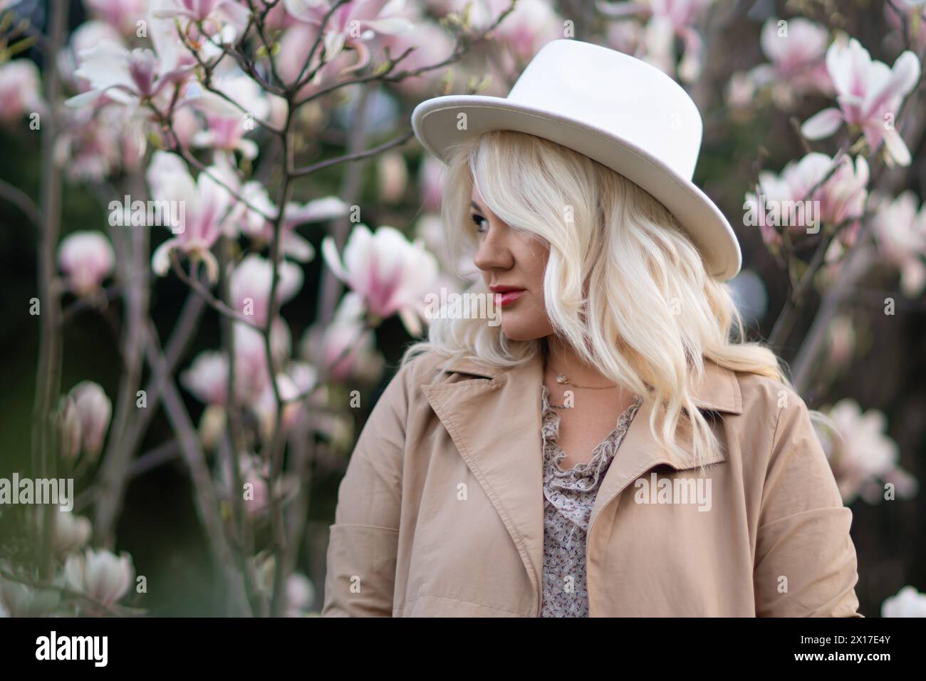 A blonde woman wearing a white hat stands in front of a tree with pink ...