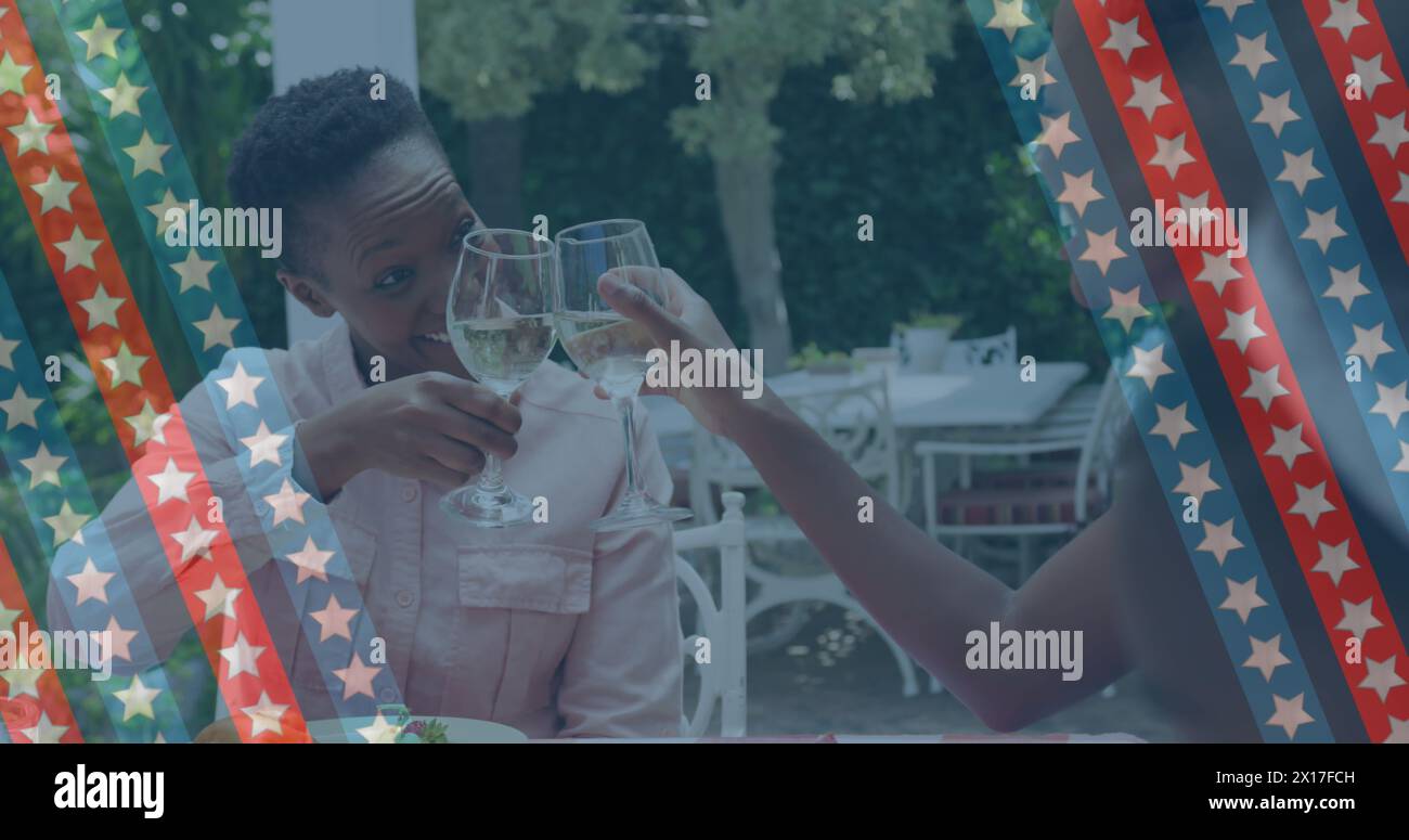 Image of stripes with stars over happy african american women drinking wine in garden Stock Photo