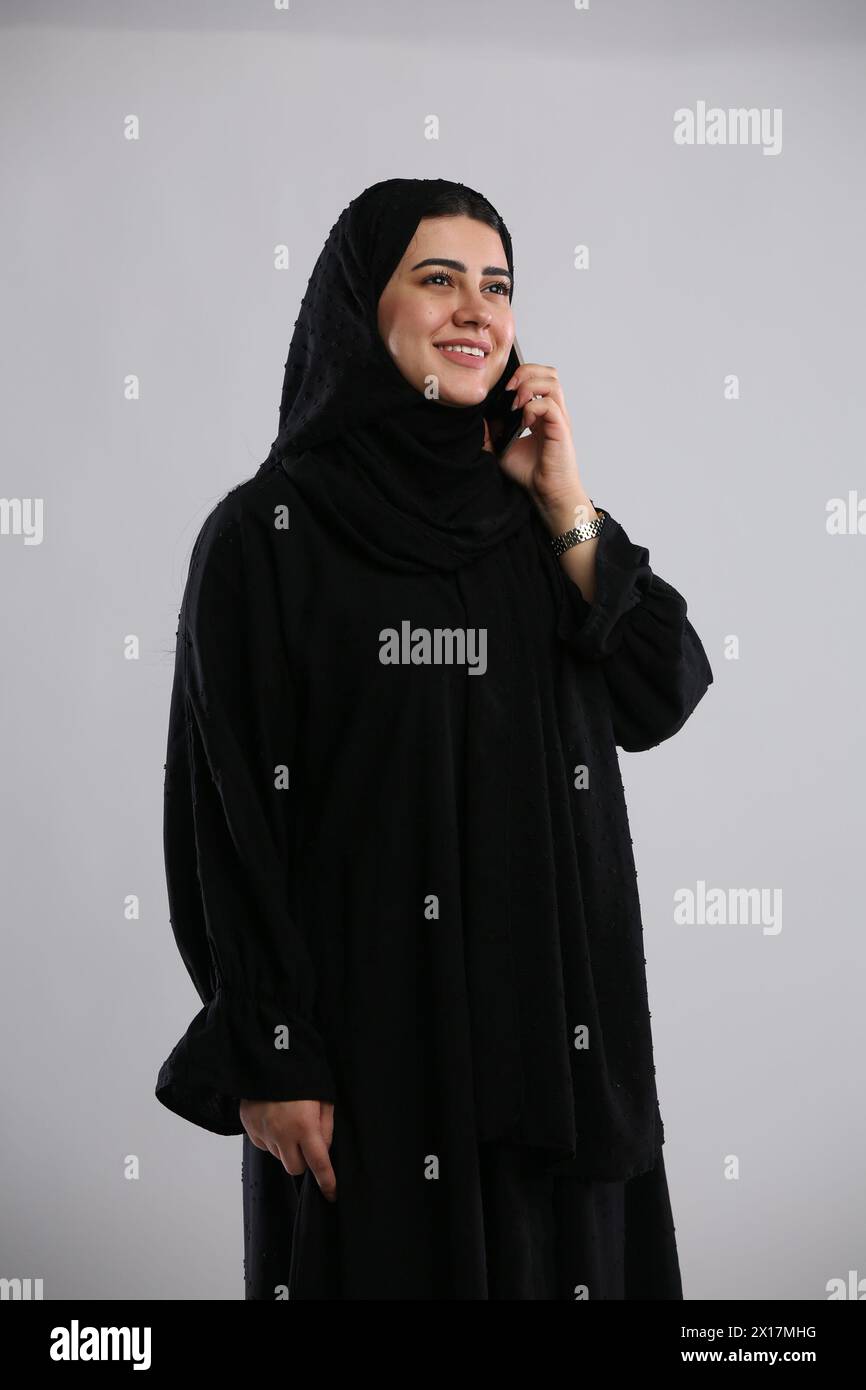 saudi arabian woman in hijaab standing with phone in hand and talking with a smile Stock Photo