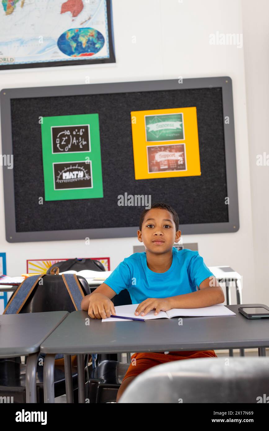 In school, young biracial boy sitting at a desk in a classroom, looking ...