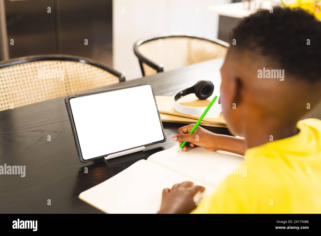African American boy writing in notebook at home, tablet with blank screen nearby with copy space Stock Photo