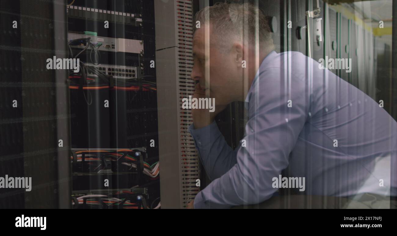 Caucasian senior male engineer talking on smartphone while working in computer server room Stock Photo
