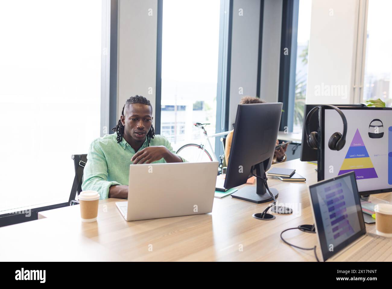 African American man with braided hair working on a laptop in a modern business office Stock Photo