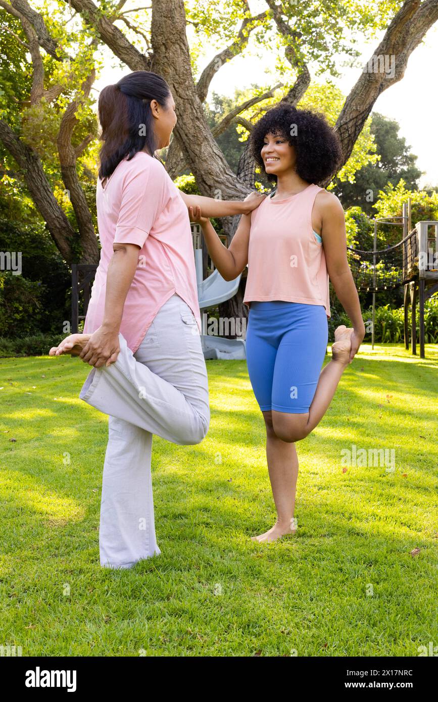Biracial mother and daughter holding hands, balancing on one foot in garden at home Stock Photo