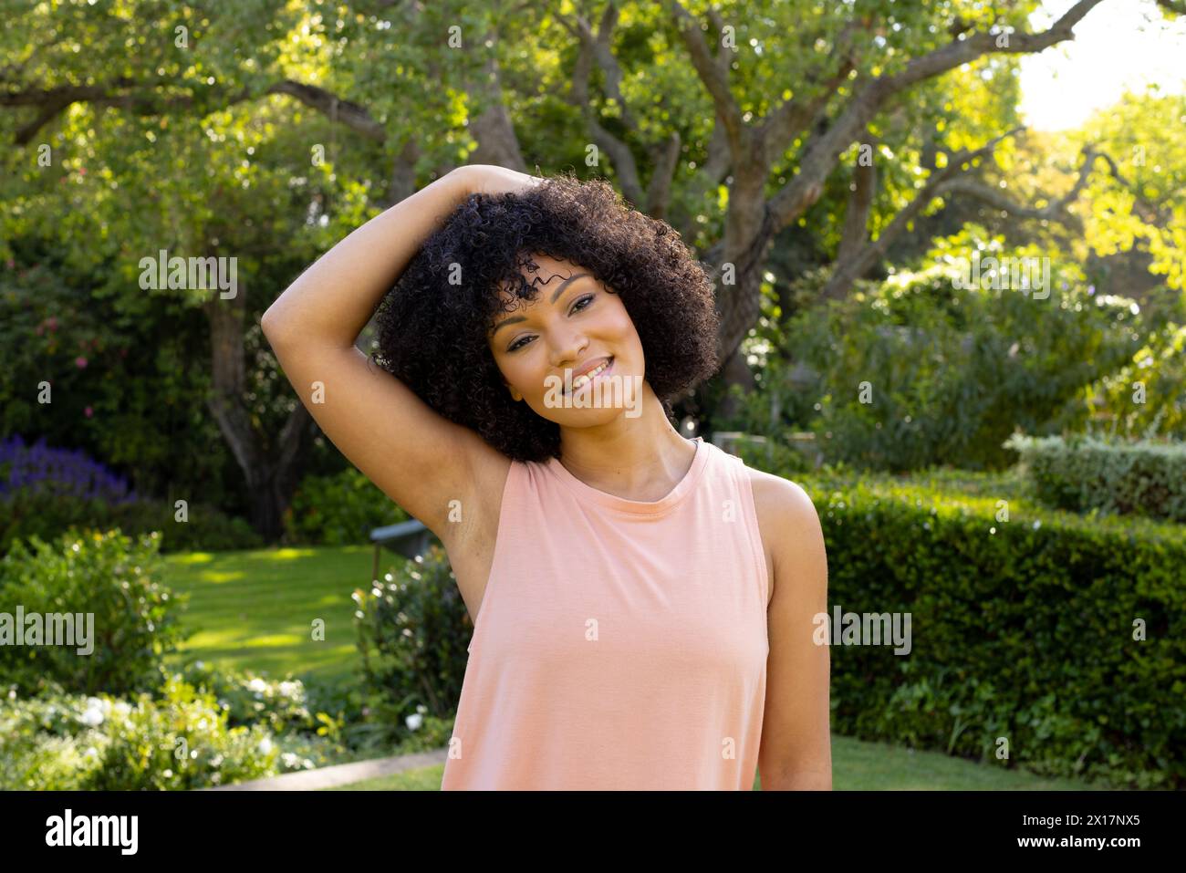 Young biracial woman standing in sunny garden at home, stretching neck, smiling Stock Photo