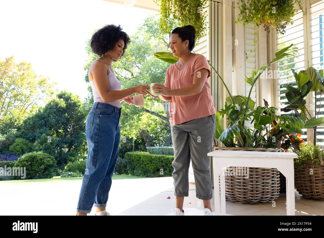 Biracial mother and adult daughter are drinking coffee outside at home Stock Photo