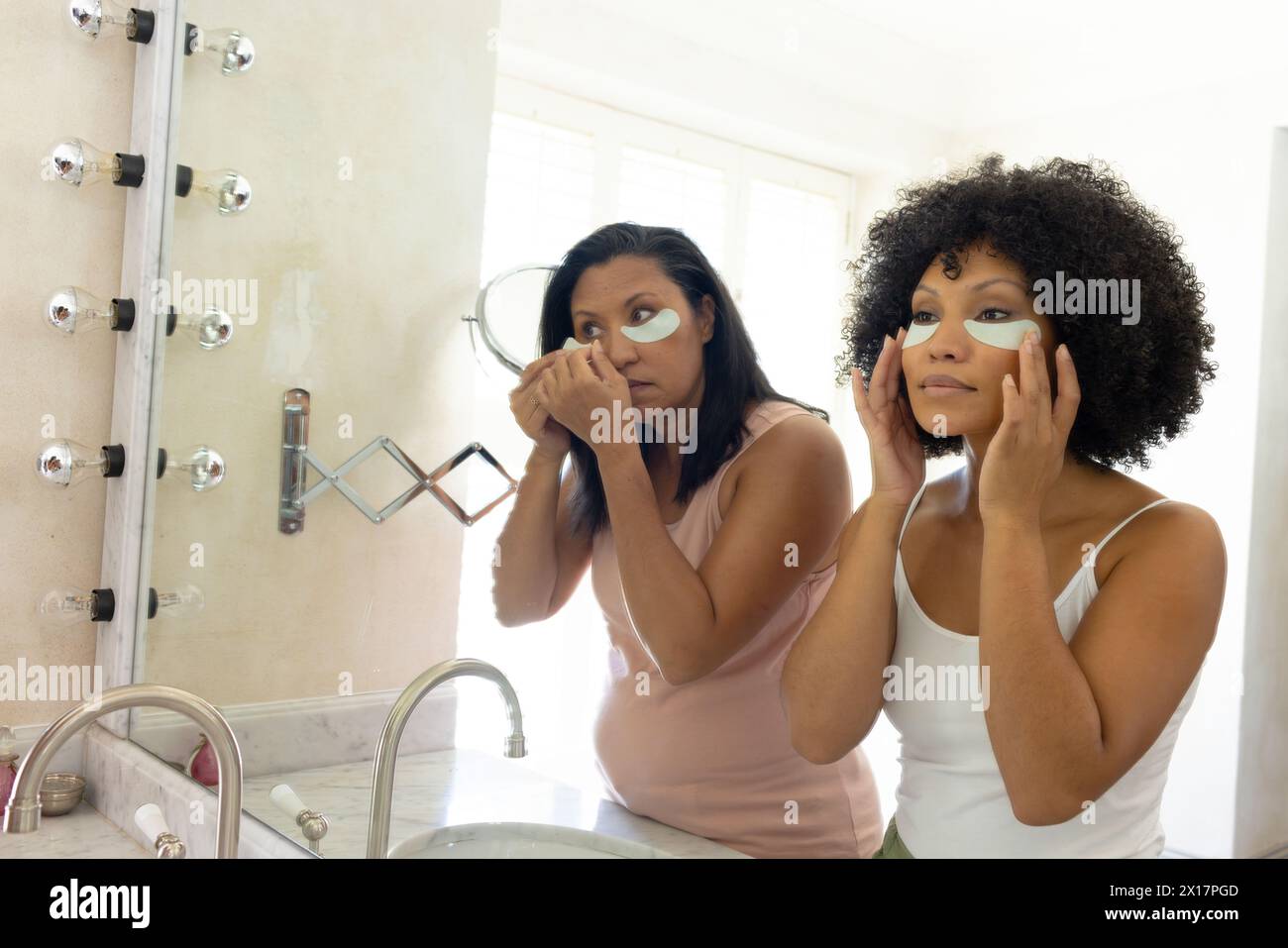 Mature biracial woman and young biracial woman applying skincare at home in the bathroom Stock Photo