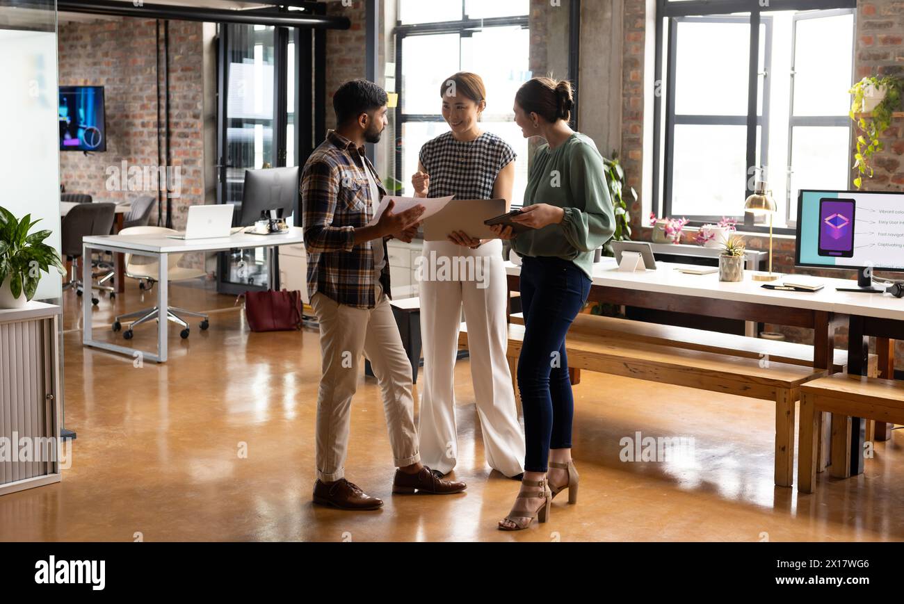 Diverse team discussing project in modern business office, mature Asian woman guiding Stock Photo