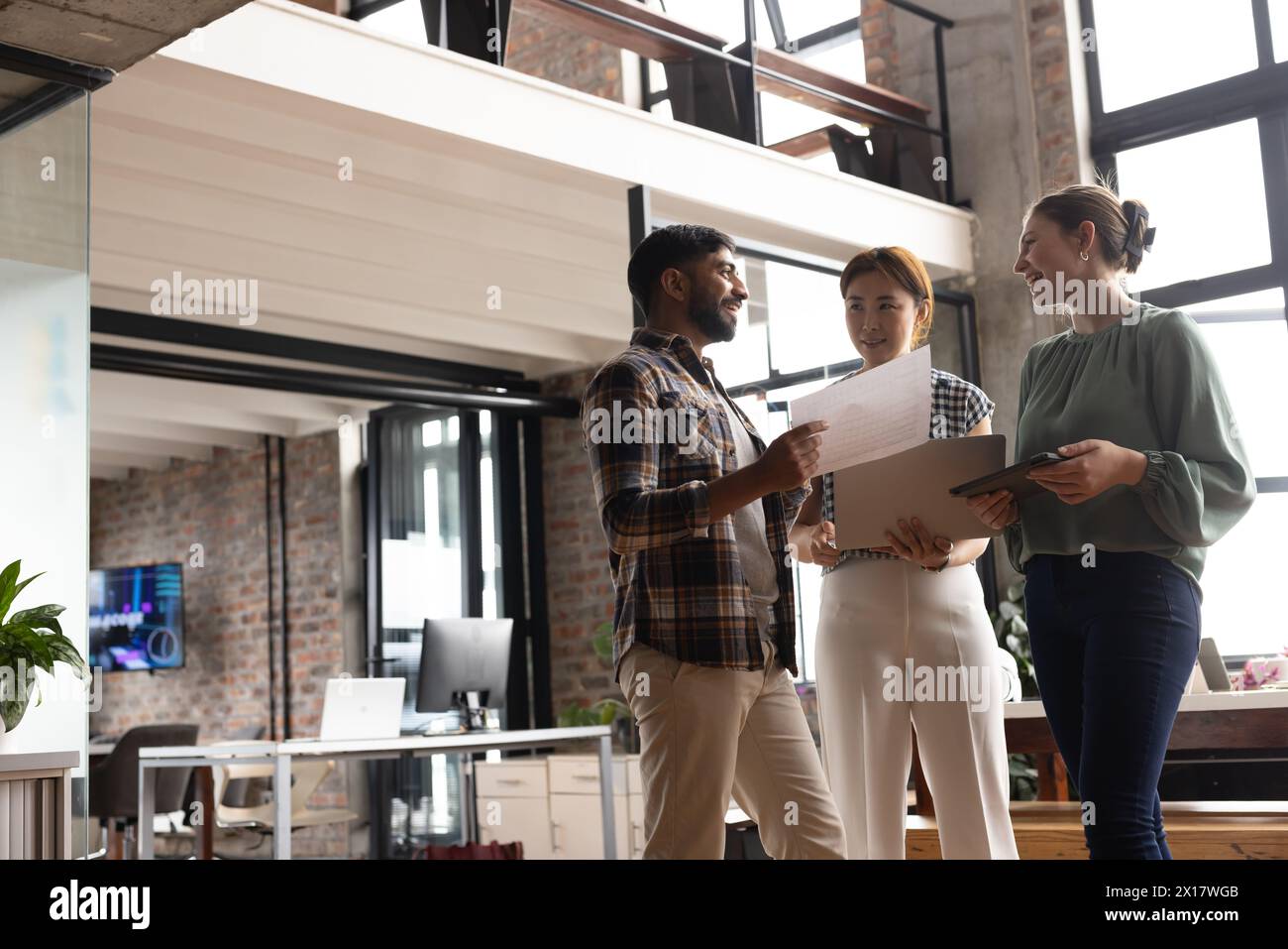 A diverse team, including an Asian mature woman, is discussing work in a modern business office Stock Photo