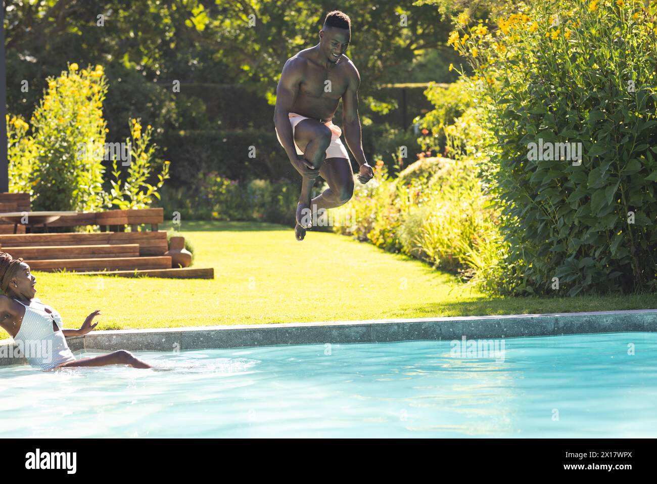 African American man jumping into pool with copy space, woman watching at home Stock Photo
