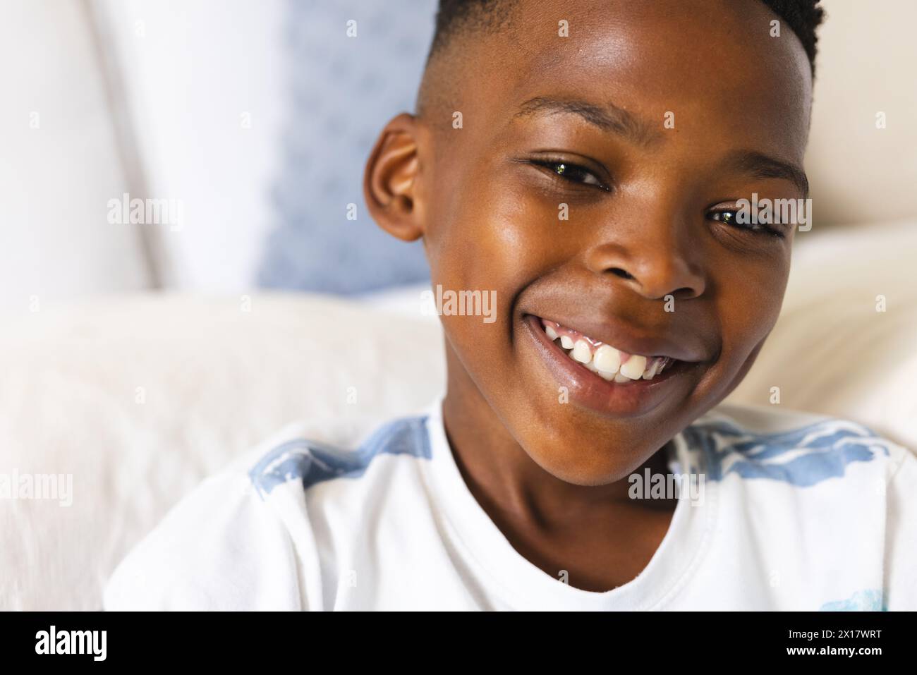 African American boy wearing white shirt is smiling at camera at home. His skin is smooth, hair short and black, eyes brown, expressing joy, unaltered Stock Photo