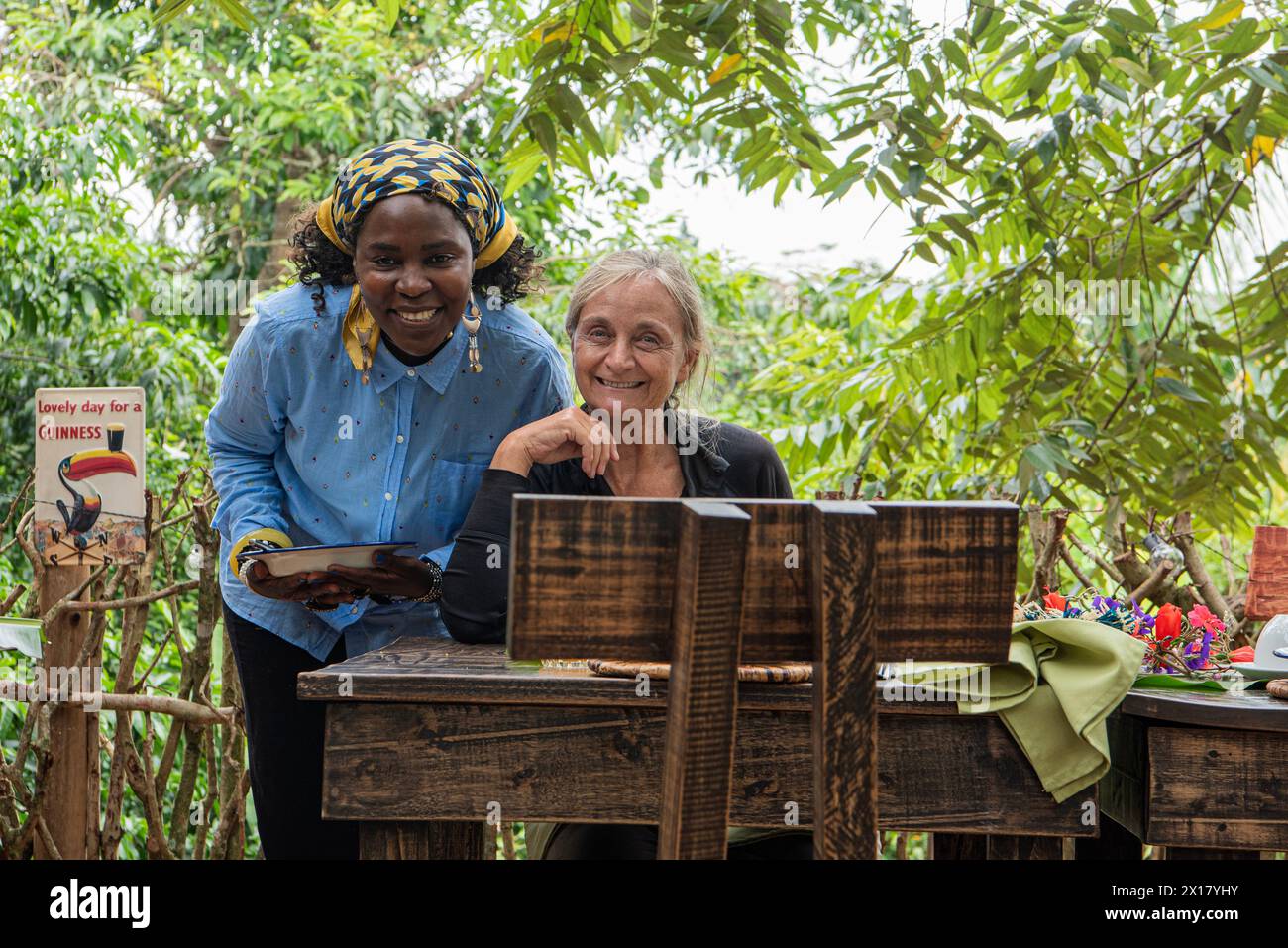 The director of Mabamba Lodge and a hotel guest share a warm, friendly pose, both smiling at the camera. The director wears a vibrant headscarf, and h Stock Photo
