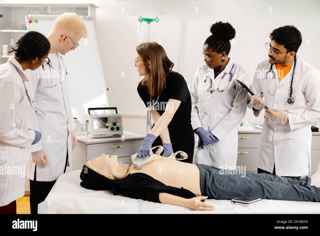 A woman lying on a bed while a group of doctors stand around her, discussing her medical condition and treatment options. Stock Photo