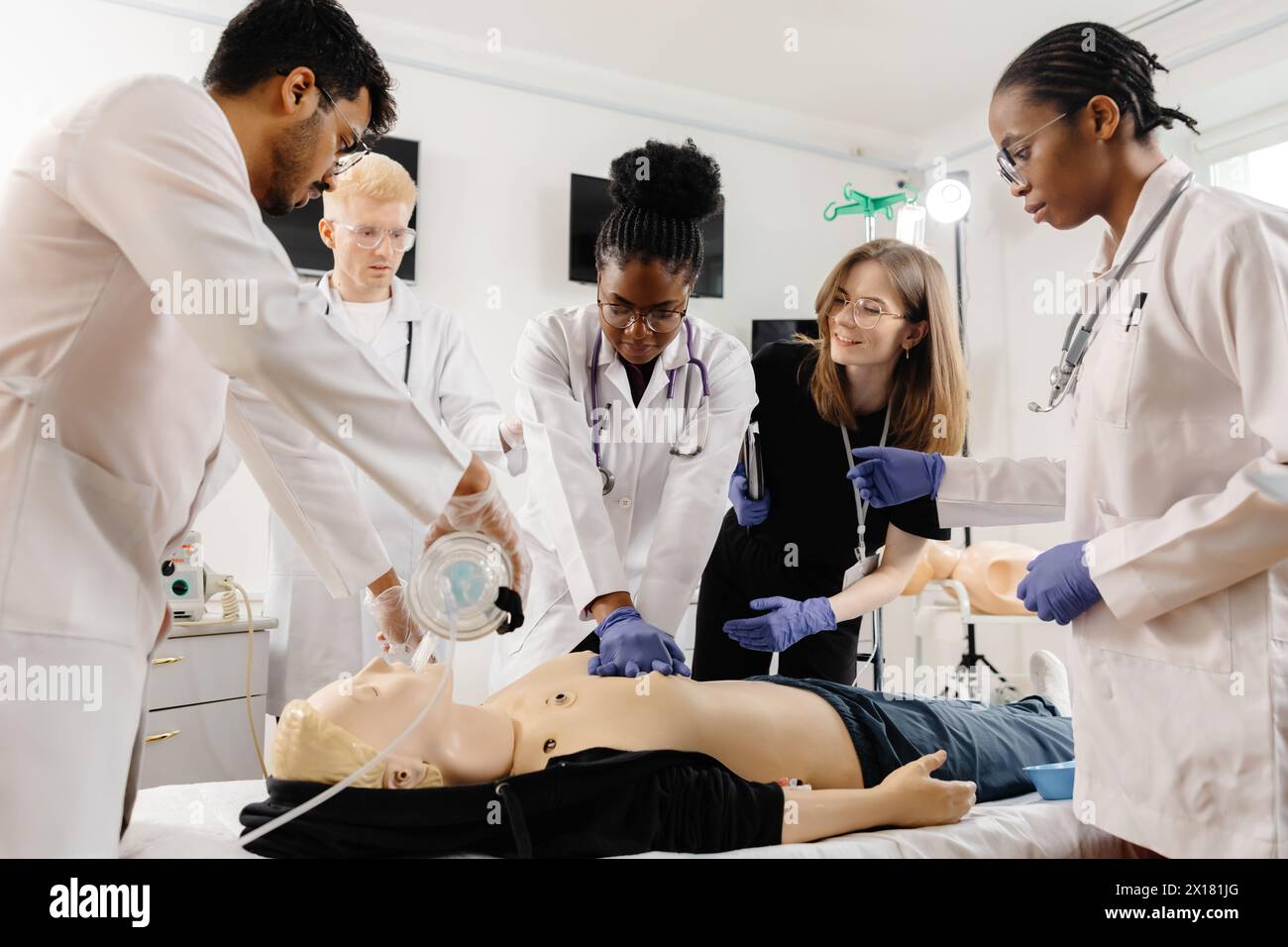A group of medical personnel is gathered around a CPR training dummy, practicing life-saving techniques in a medical simulation setting. Stock Photo