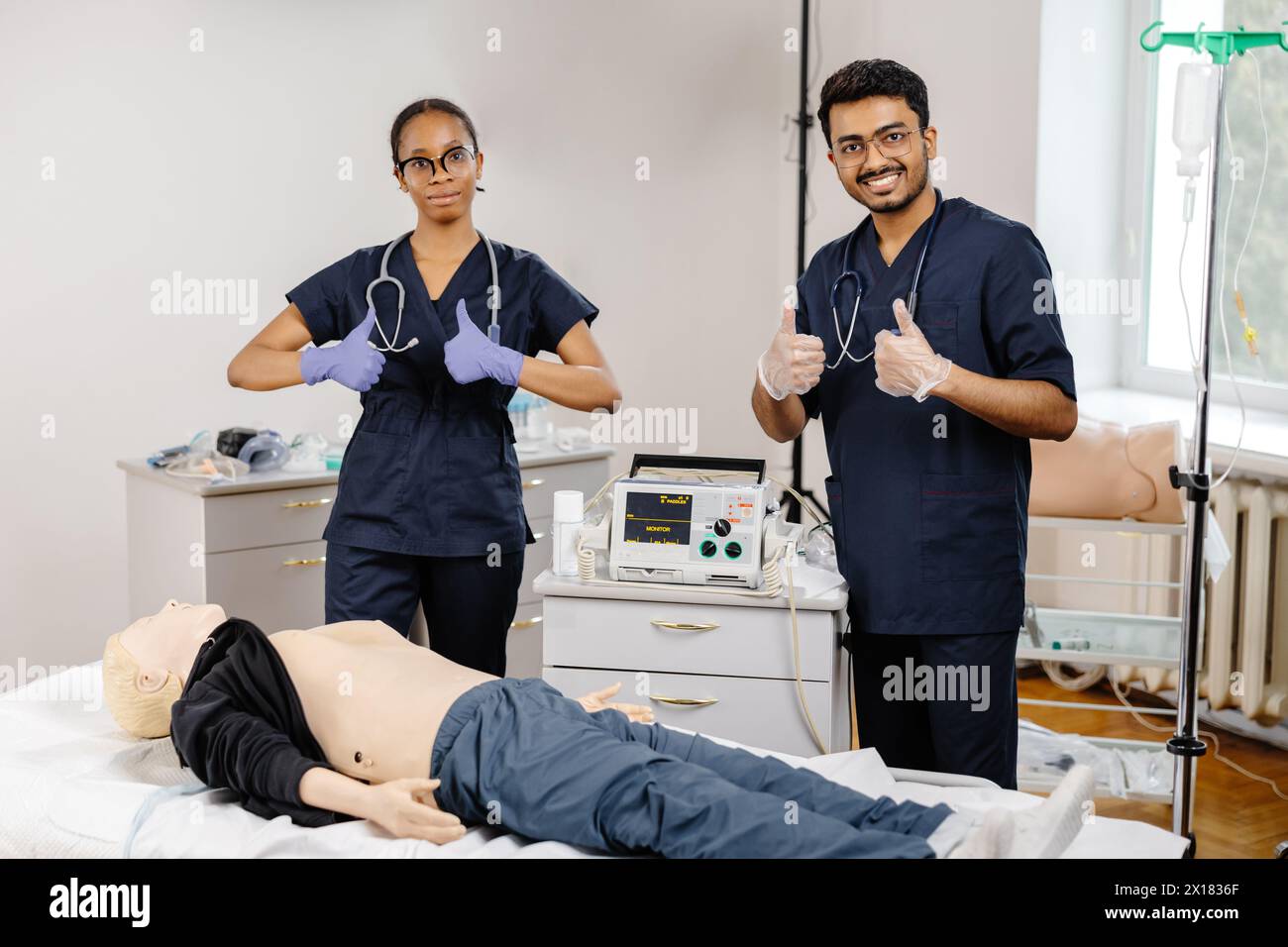 Two doctors in hospital attire standing over a medical dummy, examining and discussing medical procedures and techniques. Stock Photo