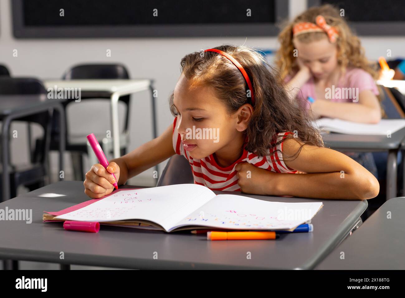 In school, young biracial female student concentrating on writing in the classroom Stock Photo