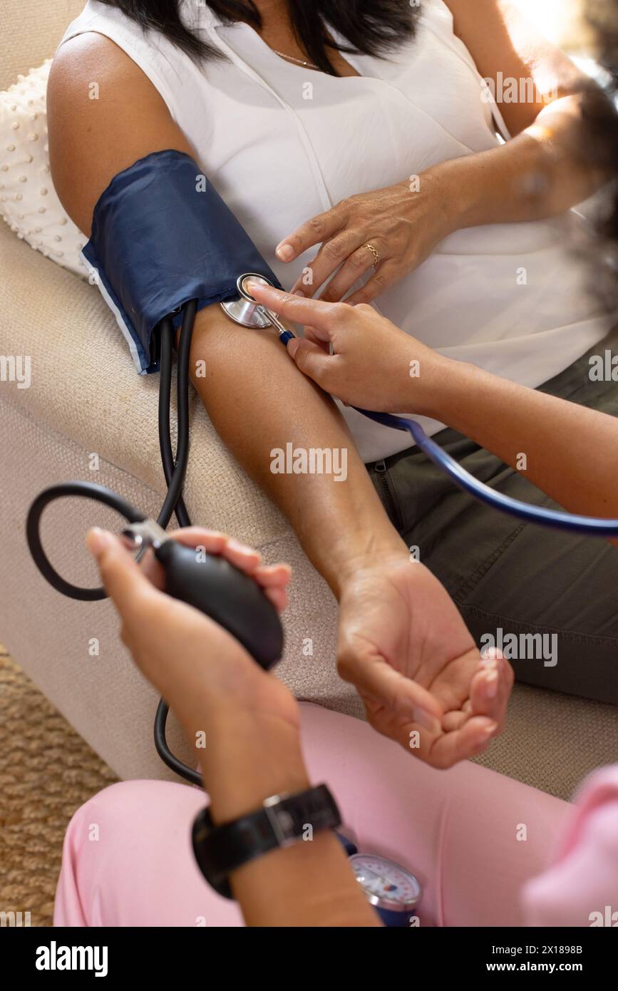 Mature biracial woman getting blood pressure checked by young biracial woman at home Stock Photo