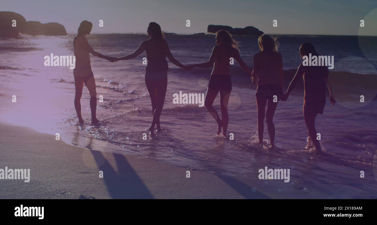 Image of glowing lights over group of female friends by the sea Stock Photo