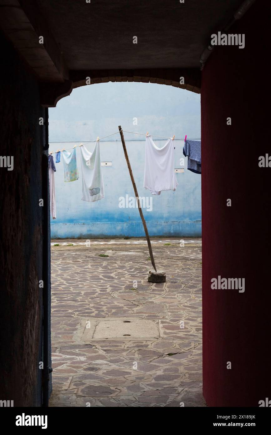 Silhouetted corridor and washed clothes on clothesline in residential backyard with flagstones, Burano Island, Venetian Lagoon, Venice, Veneto, Italy Stock Photo