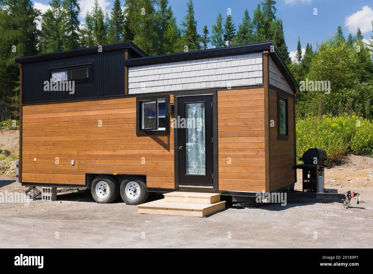 Contemporary brown stained pine and grey oak wood shingles clad cottage style 8 x 24 foot sloped roof mobile Mini House facade with black trimmed Stock Photo