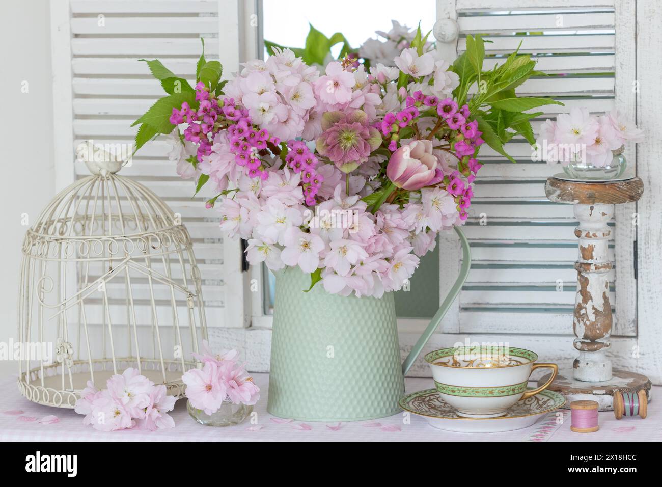 arrangement with a bouquet of Japanese flowering cherry, lenten rose, tulip and bergenia, vintage cup and bird cage Stock Photo