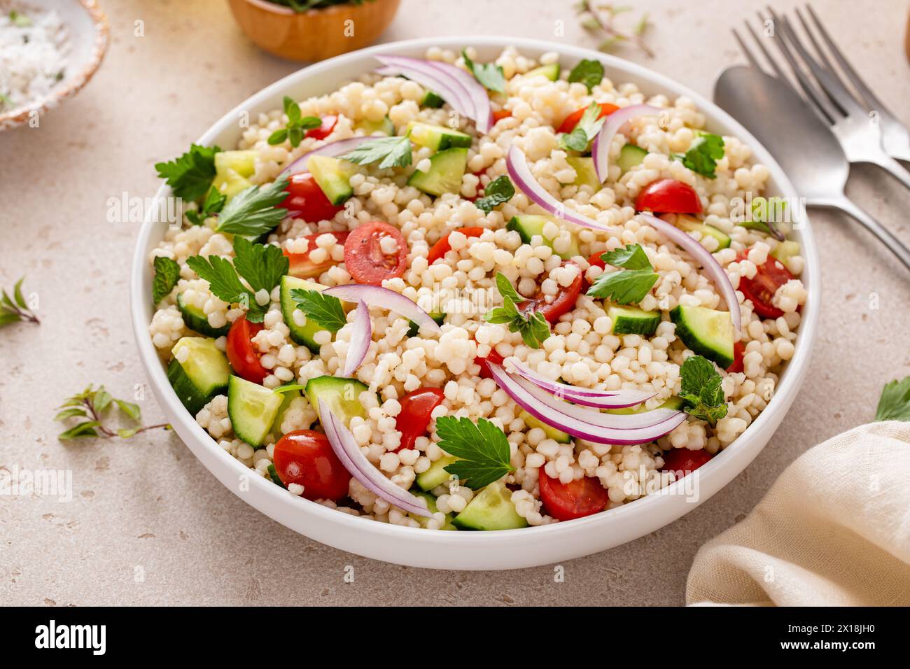 Pearl couscous salad with fresh vegetables and herbs in a serving bowl, healthy side dish idea Stock Photo