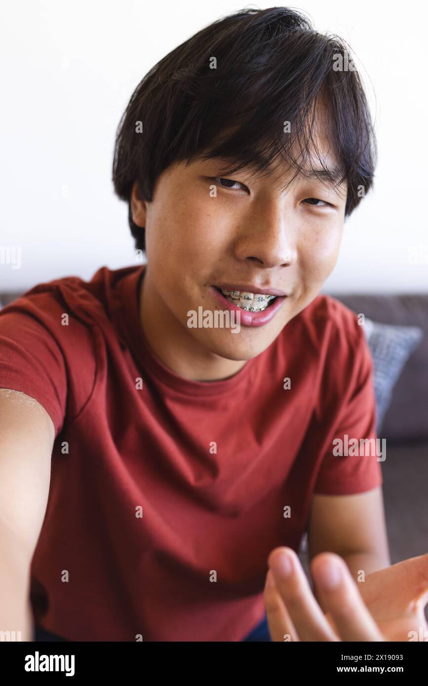 Teenage Asian boy sitting indoors, smiling at camera, having a video call at home Stock Photo