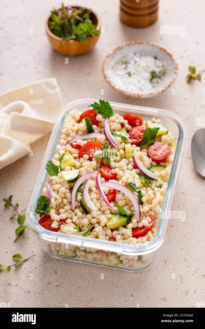 Pearl couscous salad with fresh vegetables and herbs in a meal prep container, healthy lunch or side dish idea Stock Photo