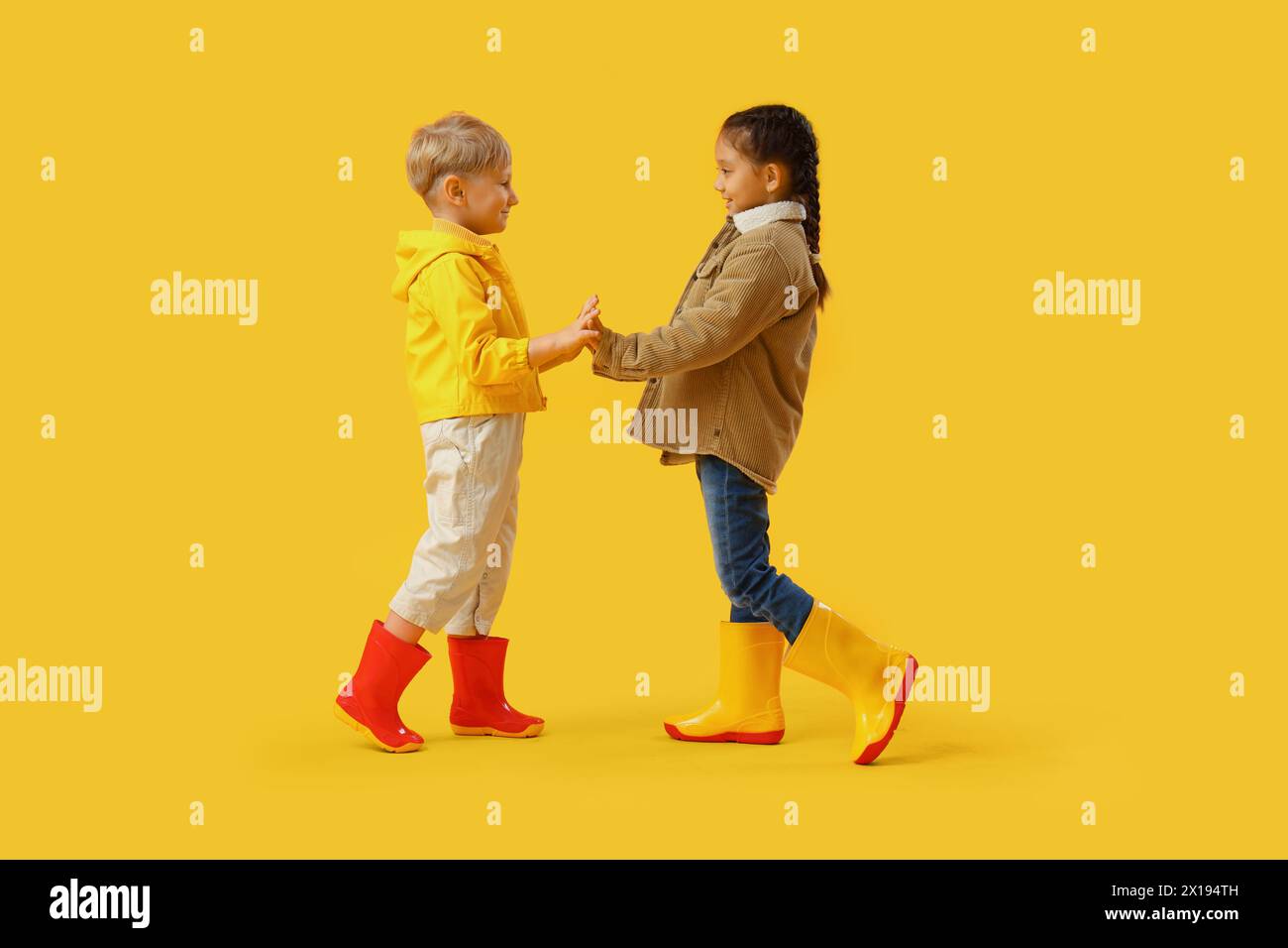 Little children in rubber boots holding hands on yellow background Stock Photo