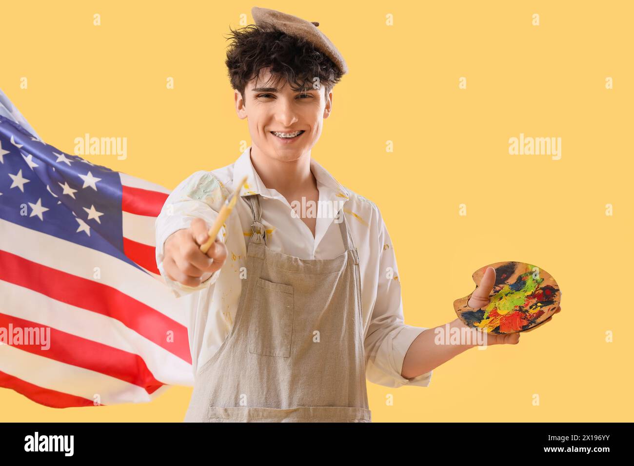 Male artist with USA flag and paint palette on yellow background Stock Photo