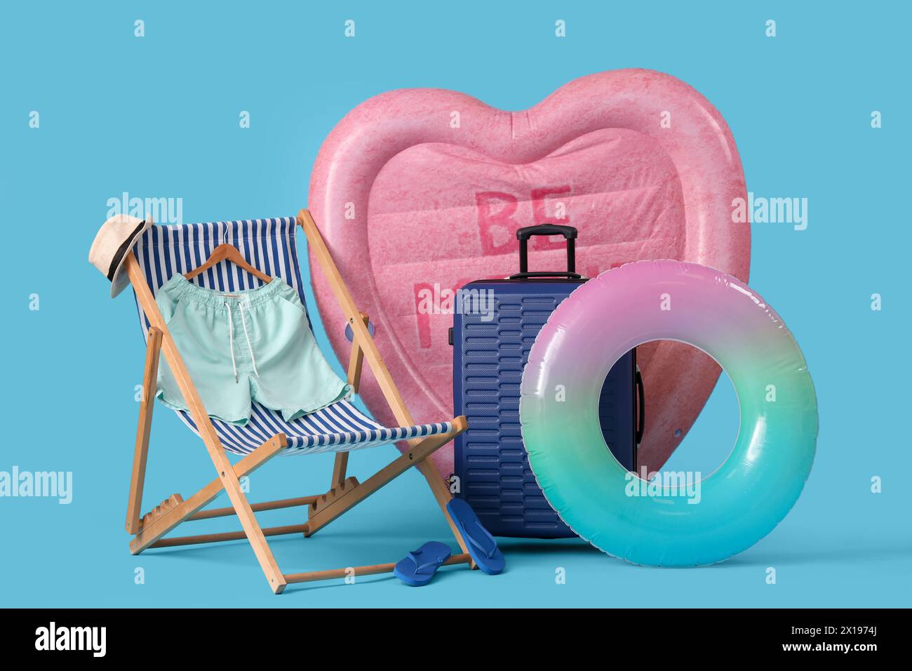 Swimming mattress in shape of heart, inflatable ring and suitcase on blue background Stock Photo