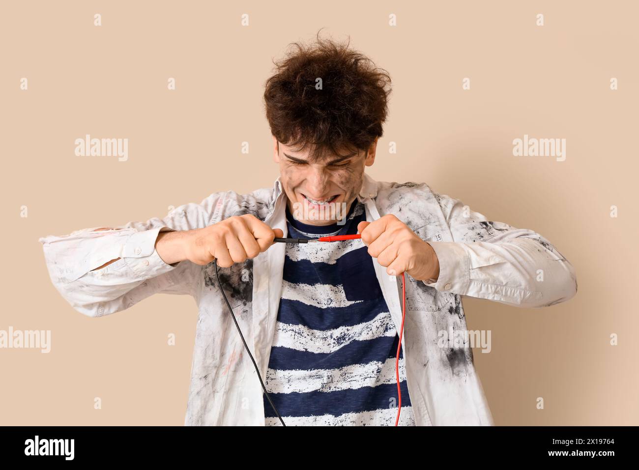 Electrocuted young man with burnt face and wires on beige background ...
