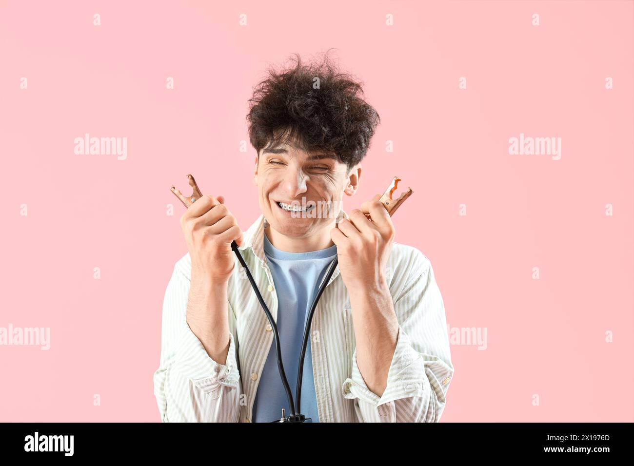 Electrocuted young man with burnt face and jumper cables on pink ...