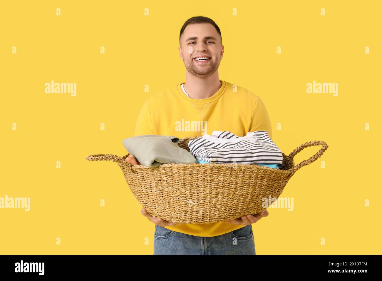 Young man holding basket with clothes on yellow background Stock Photo